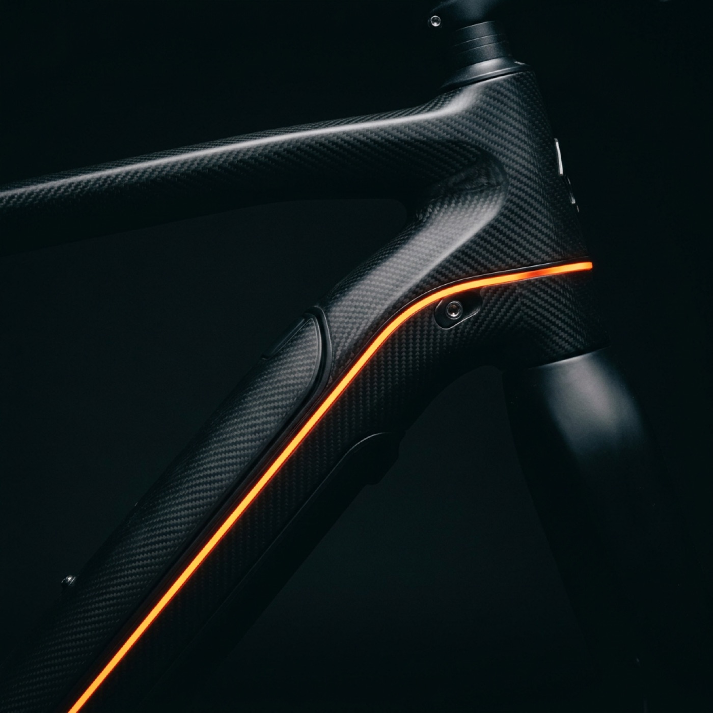 Close-up of the matte carbon head tube with a glowing orange light line running down the down tube