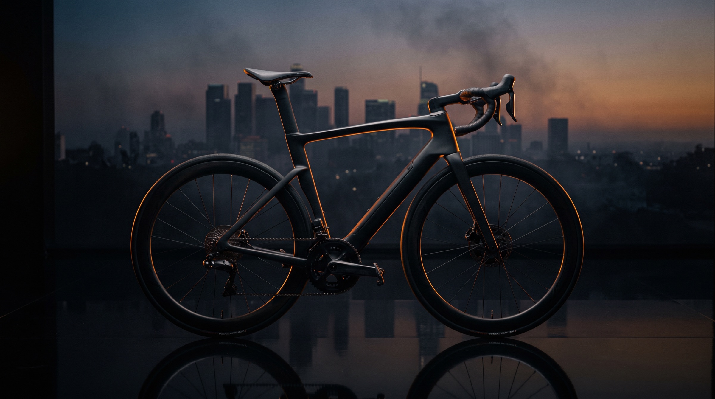 The Kestrel 01 electric road bike in matte carbon with an orange light line, standing on a reflective floor before a dusk city skyline