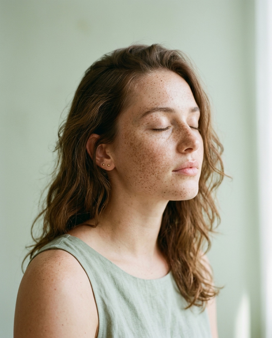 Portrait of a freckled woman with her eyes closed, calm skin in soft window light
