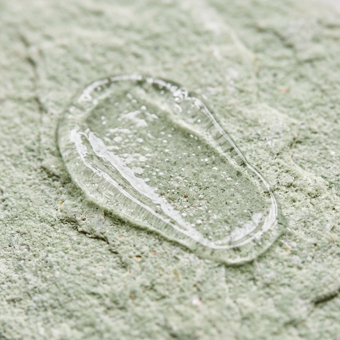 A single drop of clear gel resting on pale green mineral stone